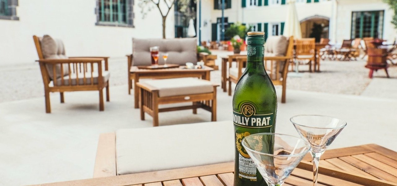 Une bouteille Noilly Prat avec deux verres posés sur une table en extérieur, invitant à savourer un verre dans une atmosphère détendue.